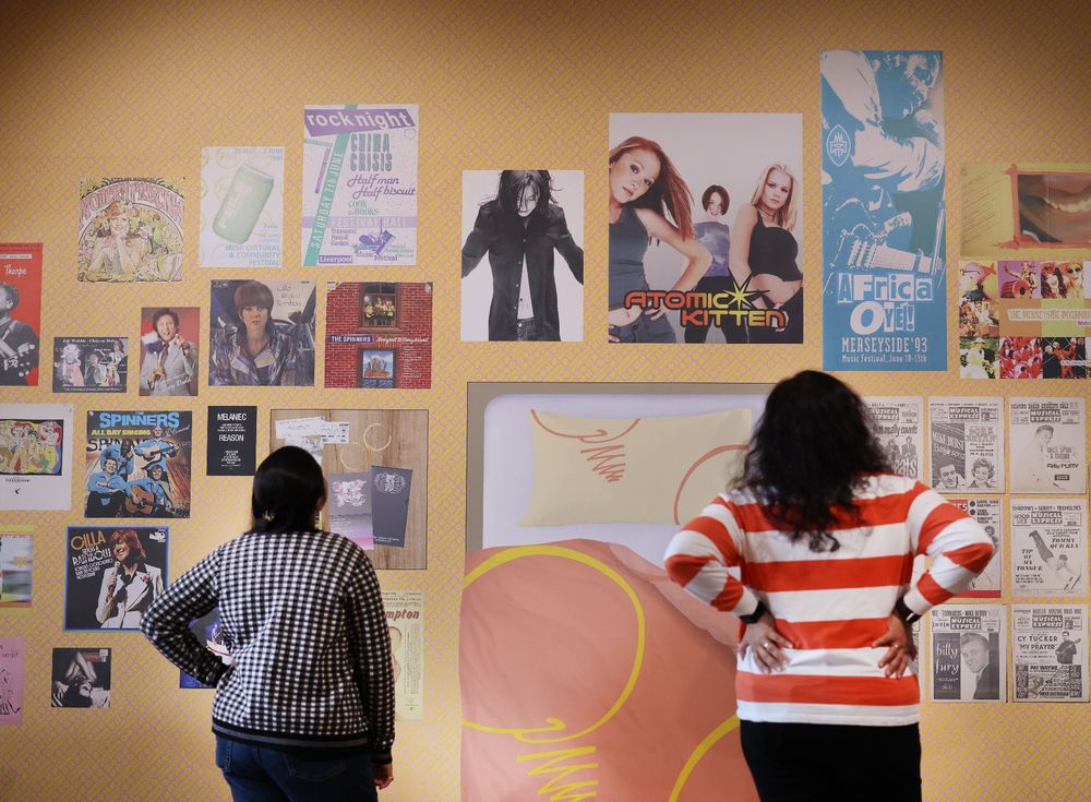 Two people look at a wall that displays posters of Liverpool popstars