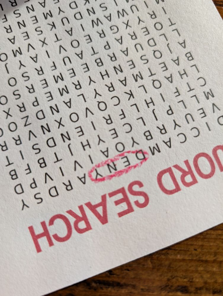 A paper copy of a scrambled letter word search, upside-down, with the letters D, E, N, and Y together inside a single red crayon circle.