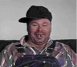 Large, scruffy man in overalls and a flannel shirt with severe dental problems and a sideways baseball cap.