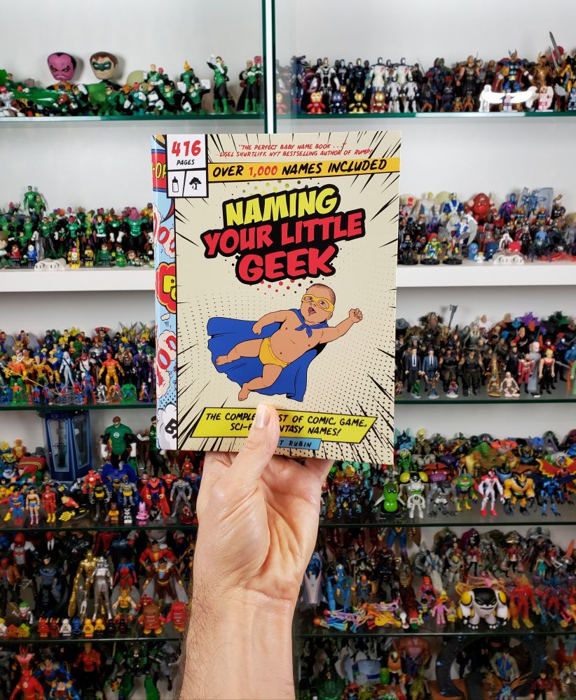 A hand holds up the awesome book Naming Your Little Geek by Scott Rubin in front of a sprawling toy collection
