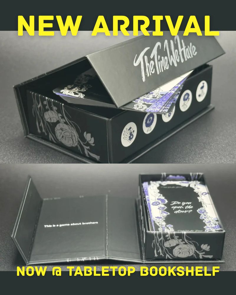 NEW ARRIVAL
The black box for the "The Time We Have", a two player game. It is at a 3/4th angle, partially open in the top image. Some of the cards are peaking out, to prop open the top of the box. 
The bottom image is the top of the box fully laid out, showcasing the cards in the box.
"Now @ tabletop bookshelf"