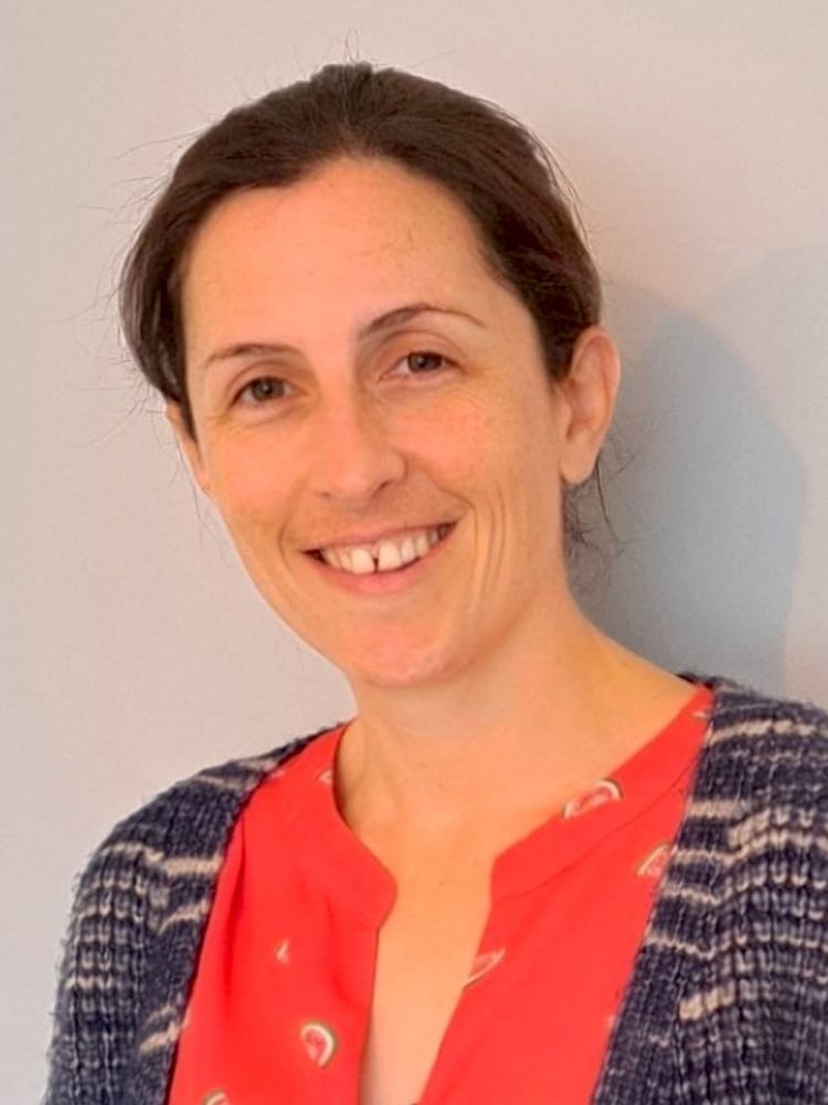 A photo of Grace facing the camera with a big smile. Her brown hair is swept back and her head is cocked to the left