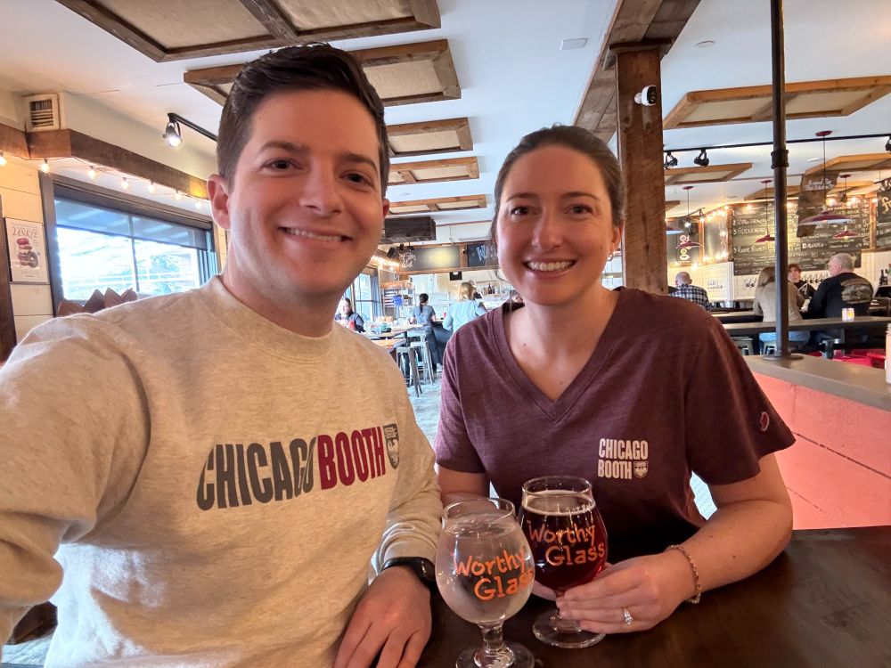 Jason and I wearing Chicago Booth swag, inadvertently looking like new MBA students. We are smiling and celebrating at a restaurant! 