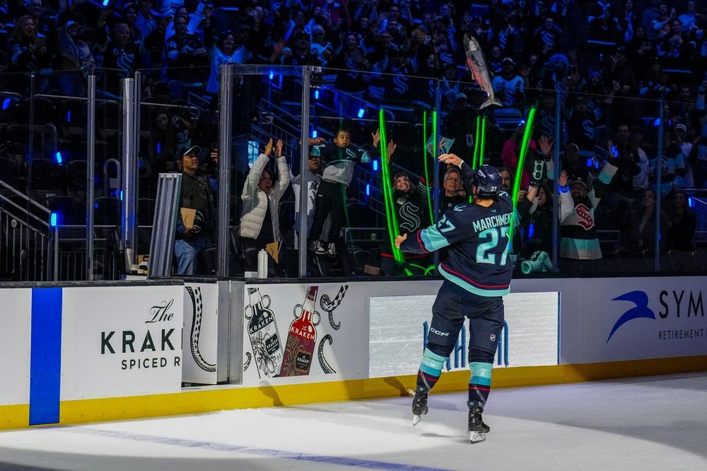 a photo of Seattle Kraken forward Mason Marchment tossing a fish over the glass.