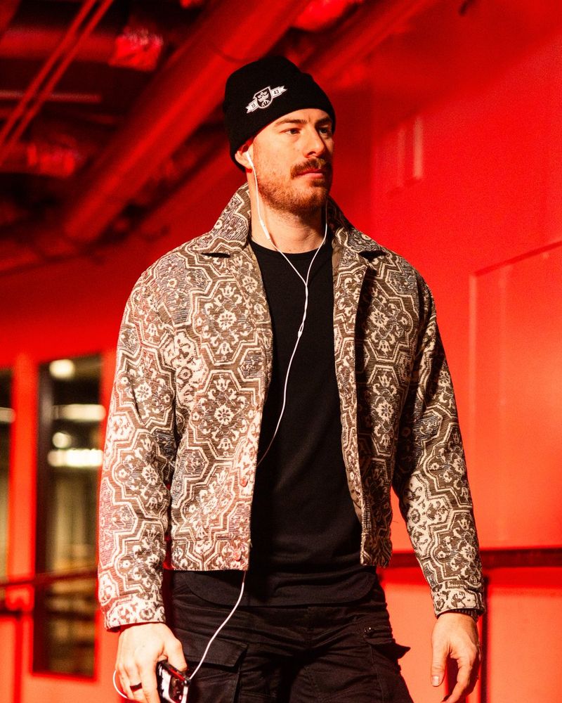 a photo of Seattle Kraken goaltender Philipp Grubauer walking into tonight's game with a wired pair of headphones in his ears. He is illuminated in red light.