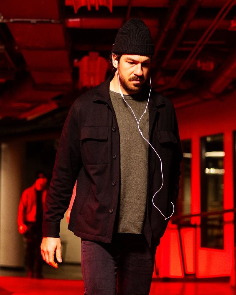 a photo of Seattle Kraken forward Freddy Gaudreau walking into tonight's game with a wired pair of headphones in his ears. He is illuminated in red light.
