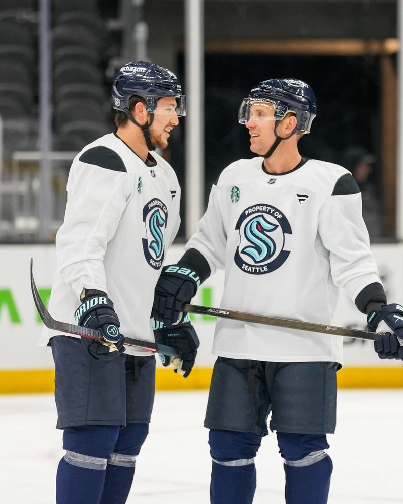 a photo of Seattle Kraken defenseman Brandon Montour and forward Jaden Schwartz chatting with each other on the ice. Both are smiling.