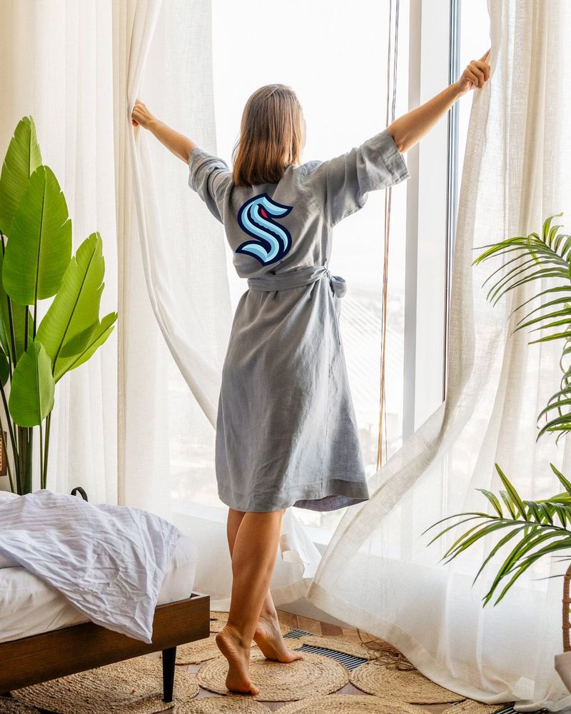 a photo of a woman pictured from behind opening the curtains. the Kraken logo is edited onto the back of her robe.