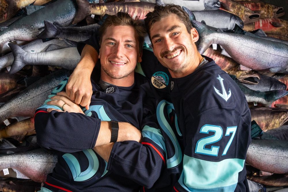 Seattle Kraken forwards John Hayden and Mason Marchment pose with their arms wrapped around each other while laying on a pile of fish.