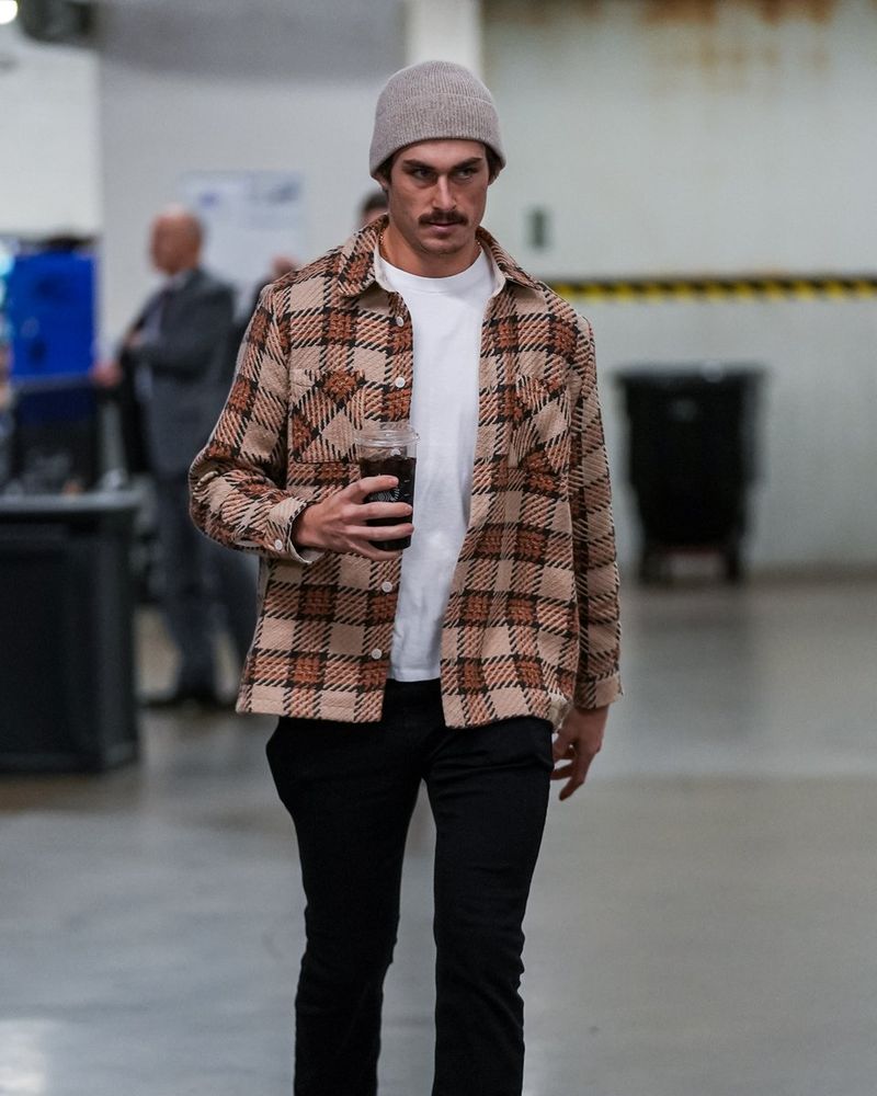 a photo of Seattle Kraken forward Mason Marchment walking into tonight's game in a brown flannel with a cup of coffee in one hand.