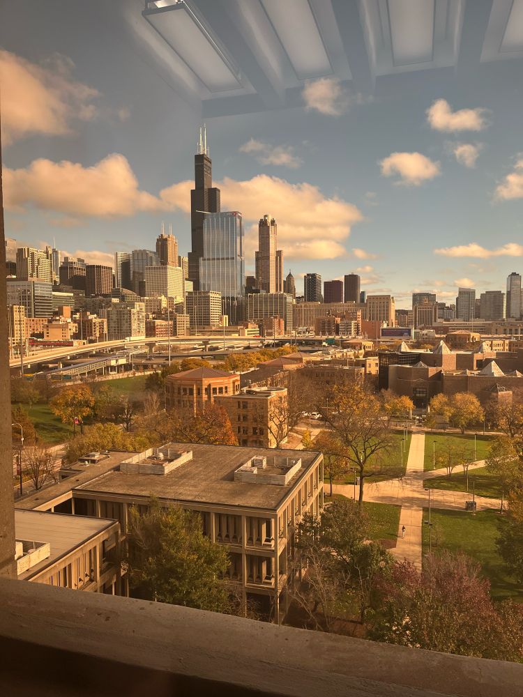 A view out a window of downtown Chicago from the west. Sears Tower is in the middle against a blue sky and the UIC quad is in the foreground. 
