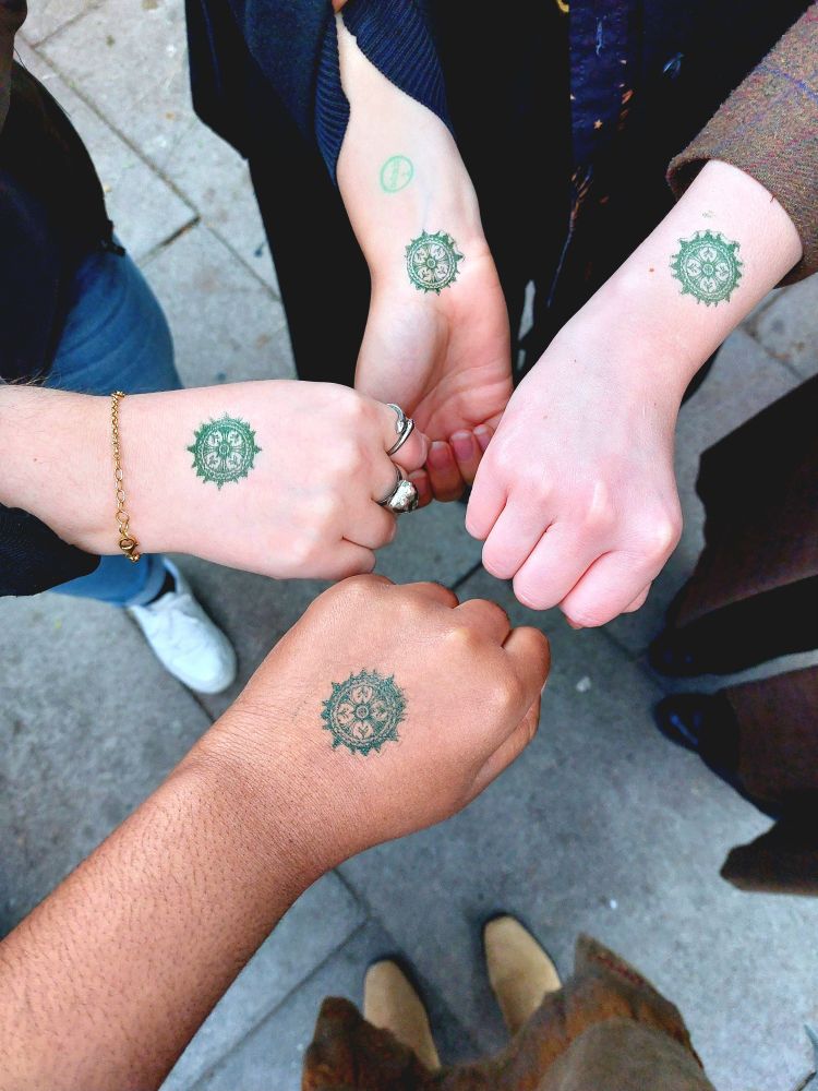 A top down picture of four hands put forward, each with a dark green yaelokre logo stamp on them. 
