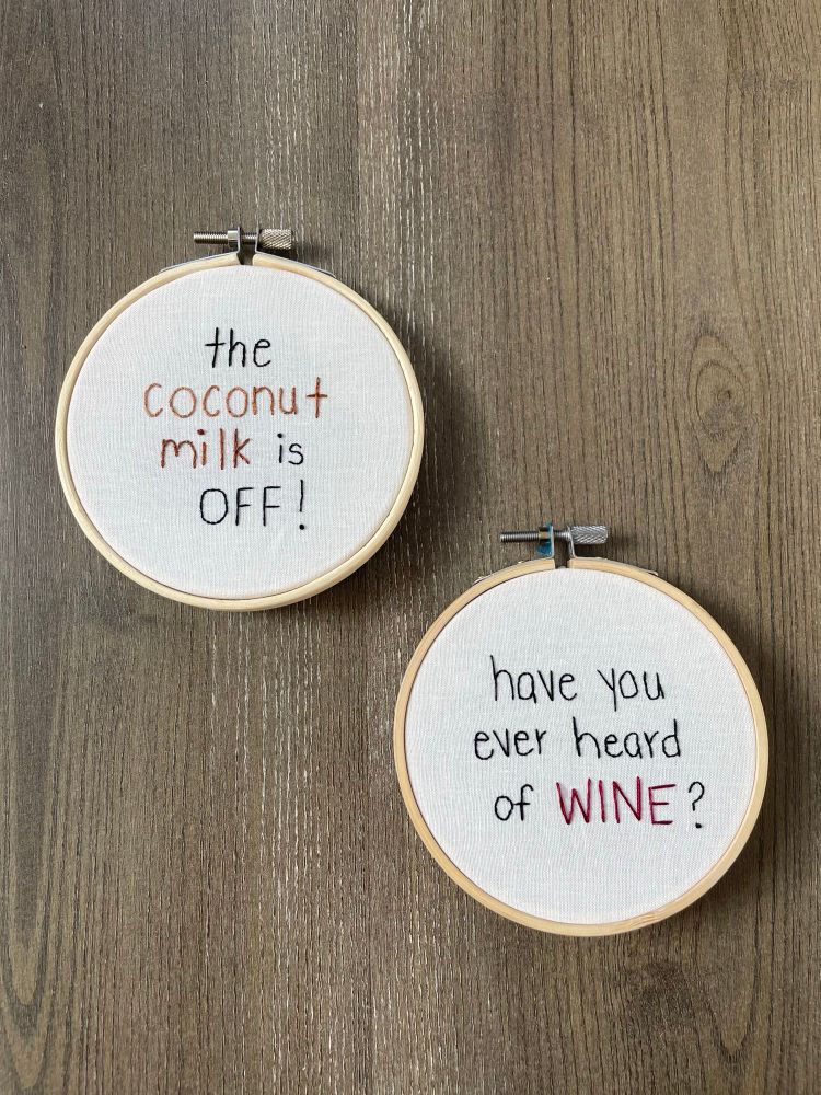 Two embroidery hoops on a wooden background. The top hoop says “the coconut milk is off” and the second says “have you ever heard of wine?”