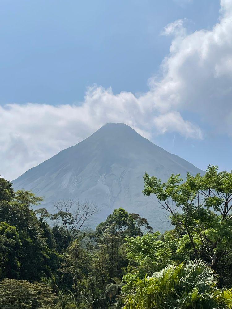 Arenal volcano, with clouds surrounding the top and trees in the foreground 
