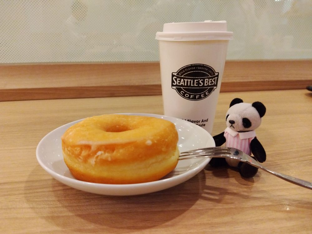 コーヒーショップ、シアトルズベストにてシュガードーナツと珈琲が並んでいる風景。片隅に小さなパンダのぬいぐるみが添えられている。