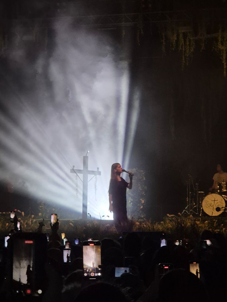 Die Sängerin ist gut ausgelichtet. Sie hält ihr Mikro in der linken Hand und steht seitlich zum Publikum. Rechts kann man den Schlagzeuger sehen.