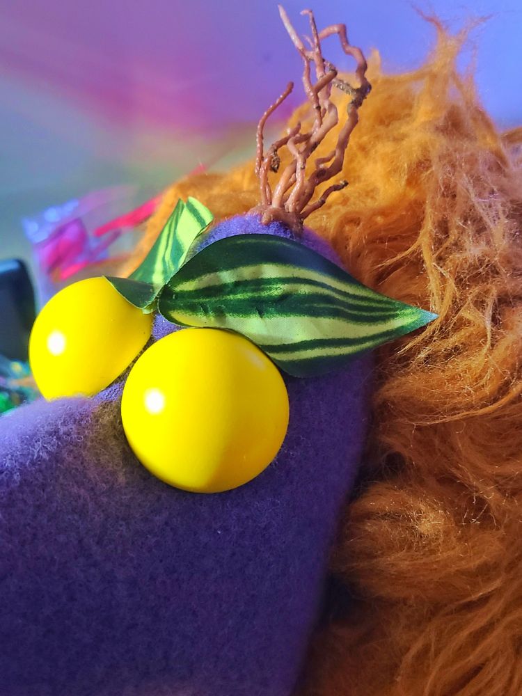 Closeup of a plant monster puppet. Big yellow eyes (before they had pupils), a big furry brown body, purple fleece skin. This puppet has a tuft of root hair and eyebrows made of leaves.