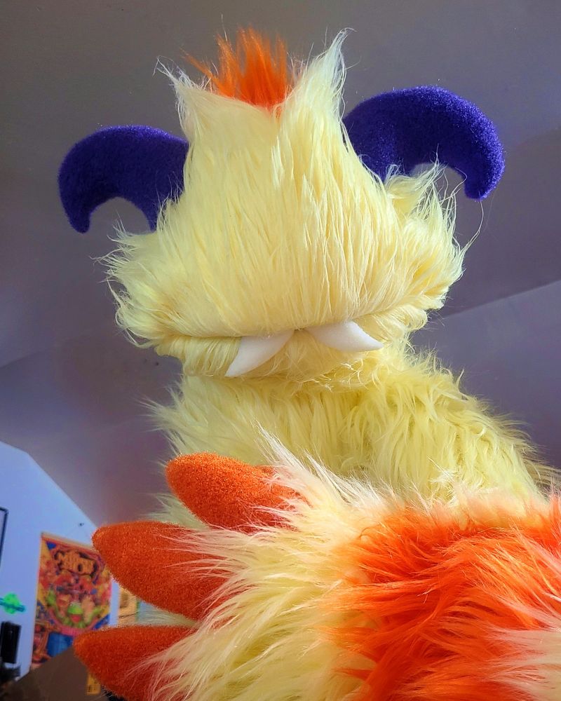 A yellow and orange monster puppet in progress. With fangs and purple horns. No eyes - it's not quite finished. 