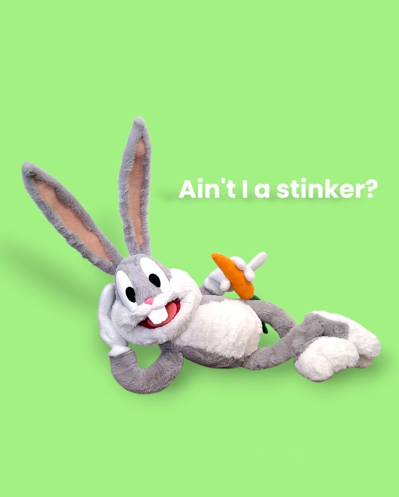 Bugs Bunny puppet built by UzzyWorks, laying on the ground with a carrot in hand. Text reads: ain't I a stinker?