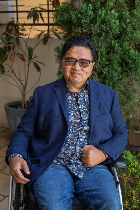 Ade Djajamihardja in a navy suit, sunnies and wheelchair outdoors