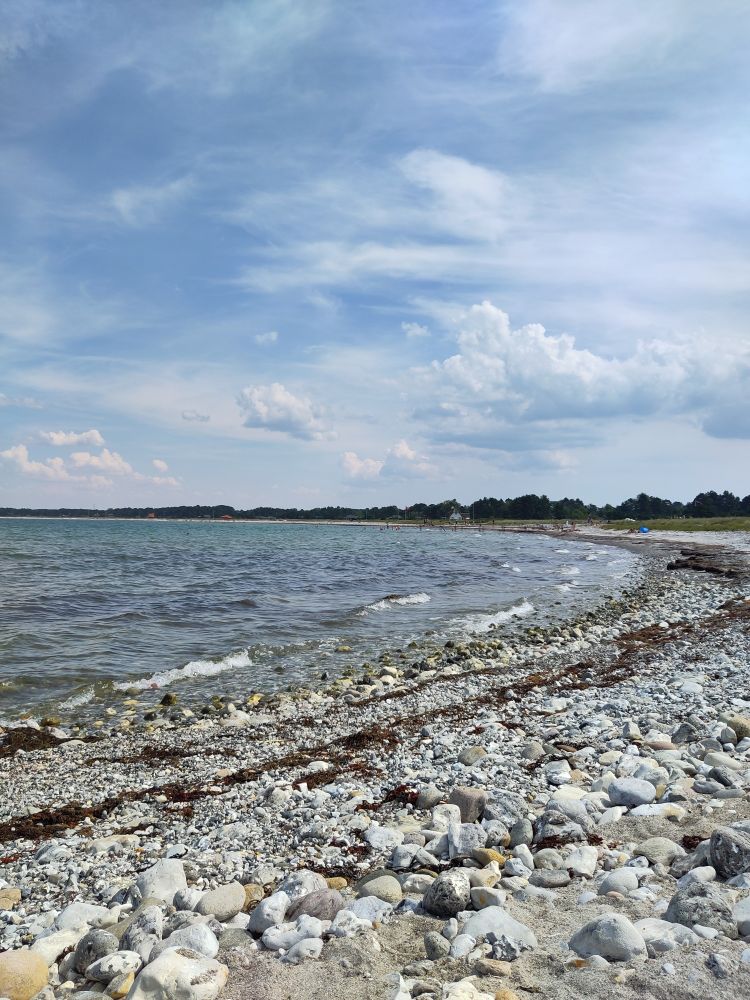 A danish beach with stones. Scattered clouds in the sky but the sun is shining 