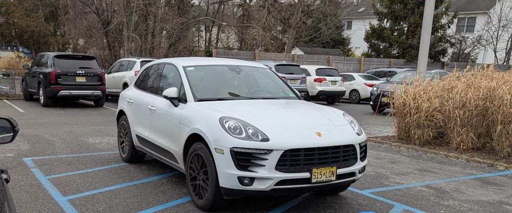 White Porsche with no handicap tag parked in between two handicap spots, where it is clearly marked as not a spot