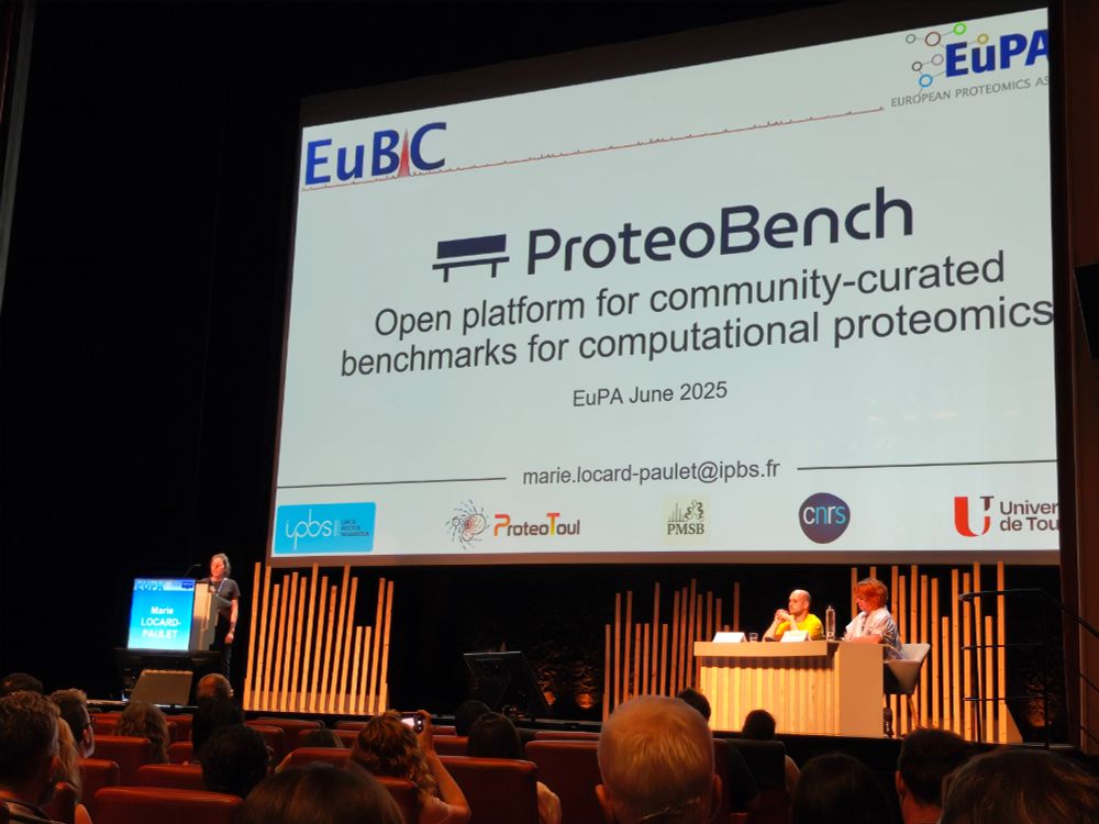Conference stage with Marie Locard-Paulet, the chairs, and the opening slide in the background.