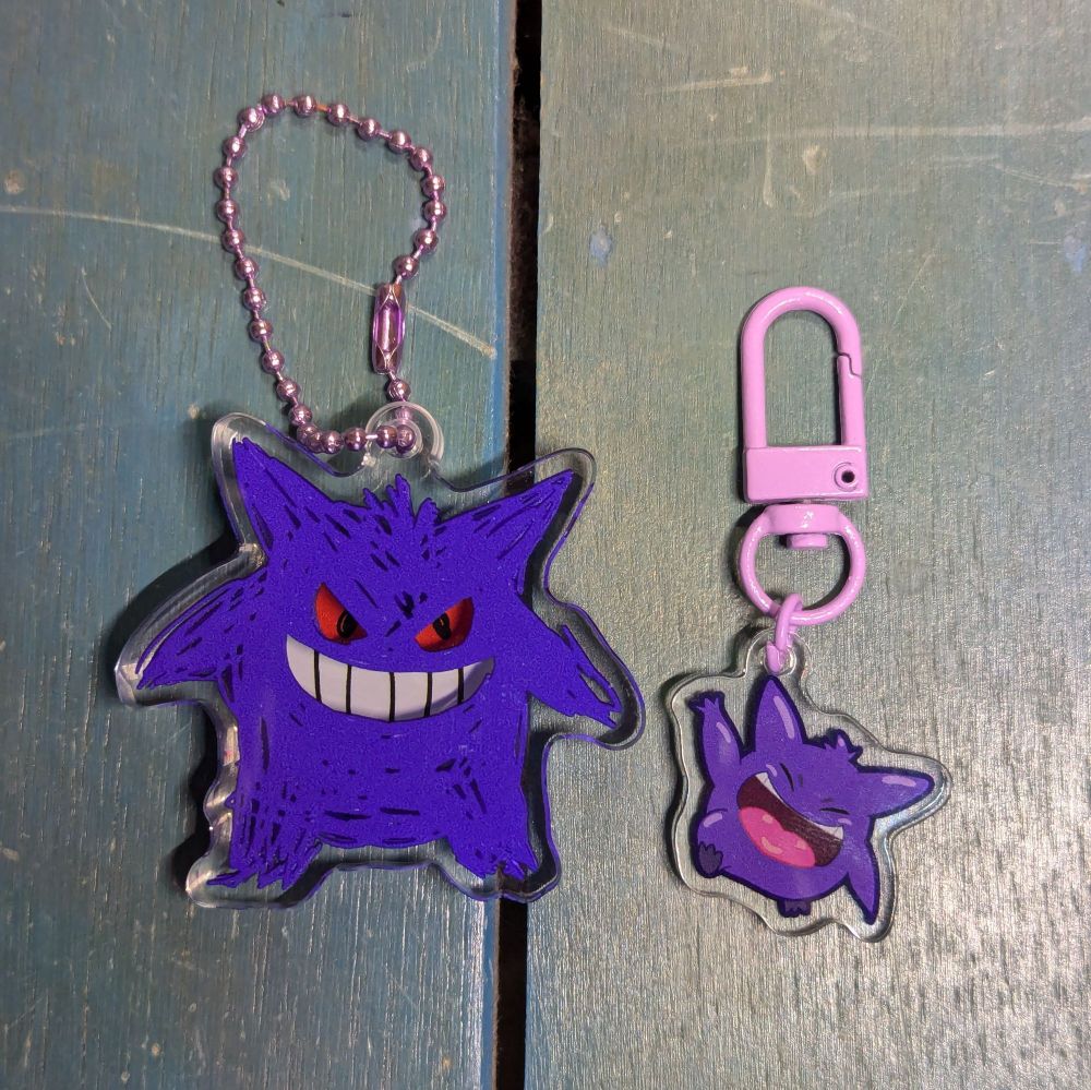 a photo of two acrylic charms, both of Gengar. the first is twice the size of the second