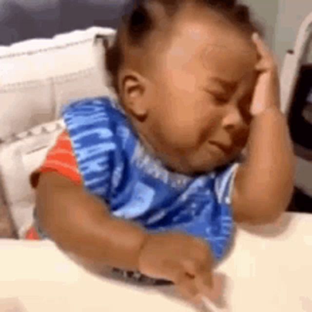 a baby is sitting at a table with his hand on his head .