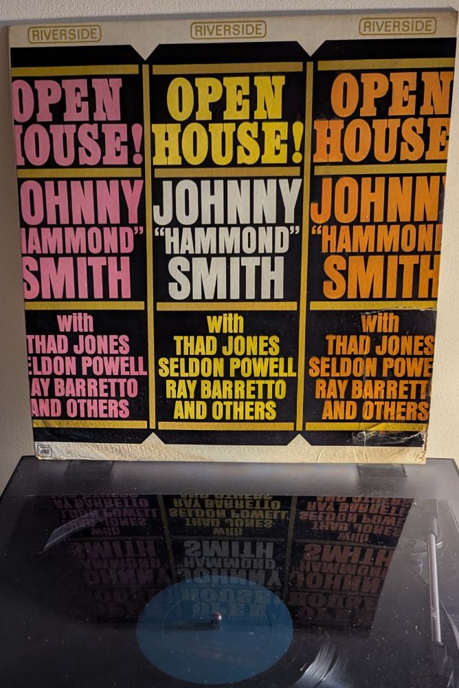 LP cover - a bit strange, this, possibly modeled after a theatrical or sports poster? Three identical panels in black with gold sticks separating the sections, the first in pink lettering, the middle in yellow and white, and the last in orange. The text is in three stacked boxes, reading OPEN HOUSE! / JOHNNY "HAMMOND" SMITH / with THAD JONES SELDON POWELL RAY BARRETTO AND OTHERS in big blocky text.