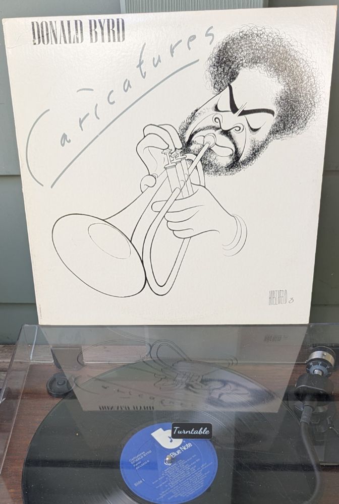 LP cover - white cover with a pen and ink illustration by Hirschfeld in his inimitable style. The head of a Black man (Byrd) playing his trumpet. He has a bushy hairstyle and beard (the latter hiding several instances of his Hirschfeld's daughter's name, Nina, as usual), angry-looking eyebrows, and flared nostrils. Maybe it's more 