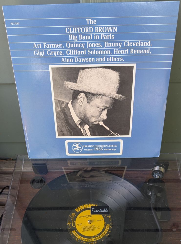 LP cover - a flat blue field, with a black and white photo of a Black man (Brownie) playing his trumpet and wearing truly spectacular hat, in a fedora style but made out of outrageously fuzzy material - angora? Wool that's only partway felted? It's spiky and hairy. Old jazz guys were so damn cool. Above the photo is the title and some of the players, in white; at the bottom, also in white, it says PRESTIGE HISTORICAL SERIES, Original 1953 Recordings.