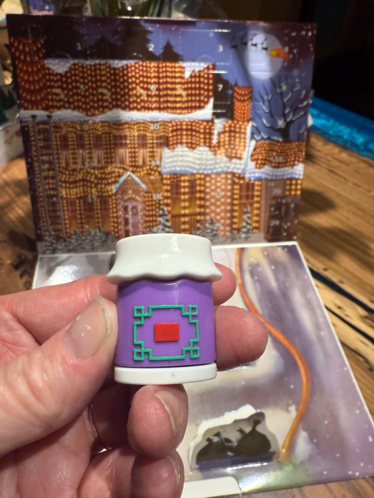 A plastic jar of jelly (of the month club). It is bright purple with a singular squiggly design on the front that is supposed to be a label. 