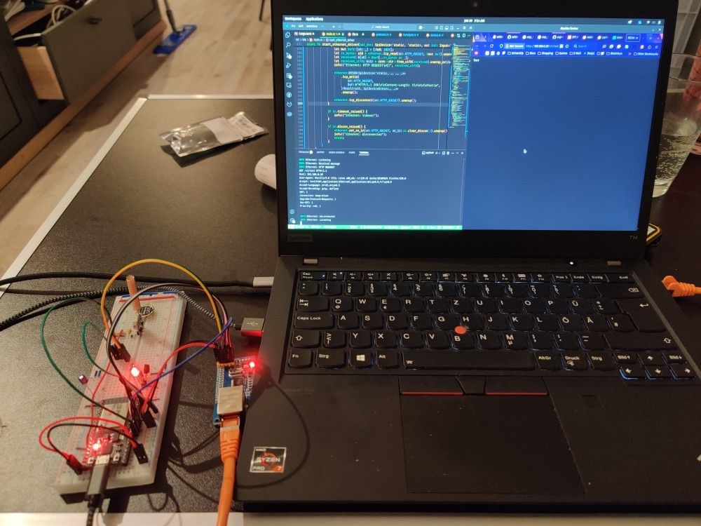 My ESP32 on a breadboard connected to the W5500 board next to my laptop. The laptop is showing VS code with the relevant code and console open, and Firefox showing a webpage hosted on the ESP32.
