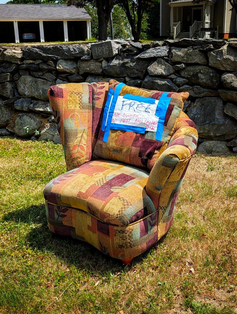 Photo of a colorful armchair with distinctive asymmetric 1990s styling. It has been placed on a sunny grassy curb with a handlettered "FREE" sign placed on the backrest. 
