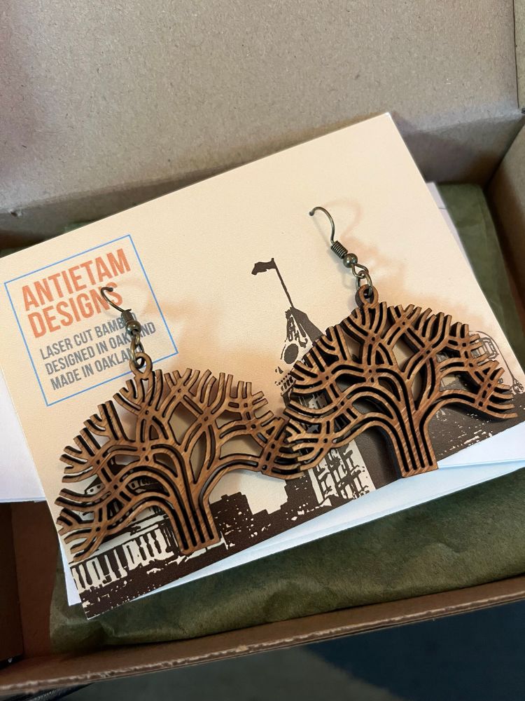 Photo of laser cut dangle earrings in the shape of the city of Oakland tree logo. They are made by Antietam Designs.
