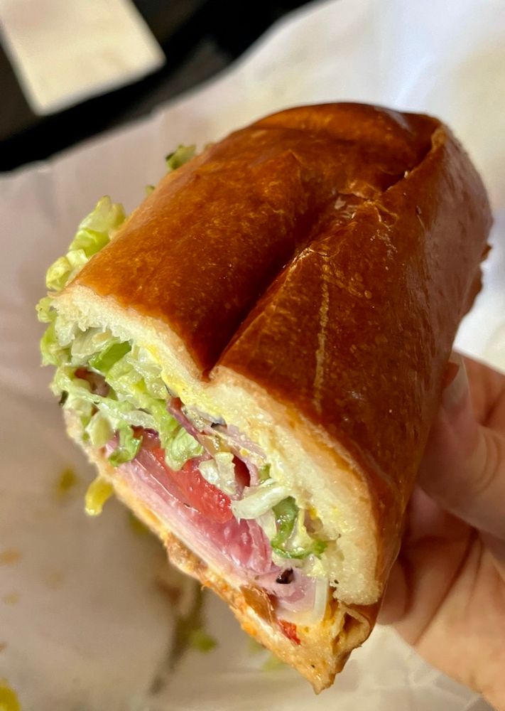 photo: closeup of one half of the "Italian Combo": 
mortadella, salami, ham, provolone, lettuce, tomato, onion, cherry pepper relish, mustard, mayo, pepperoncini and herb dressing on a Po'boy Roll.