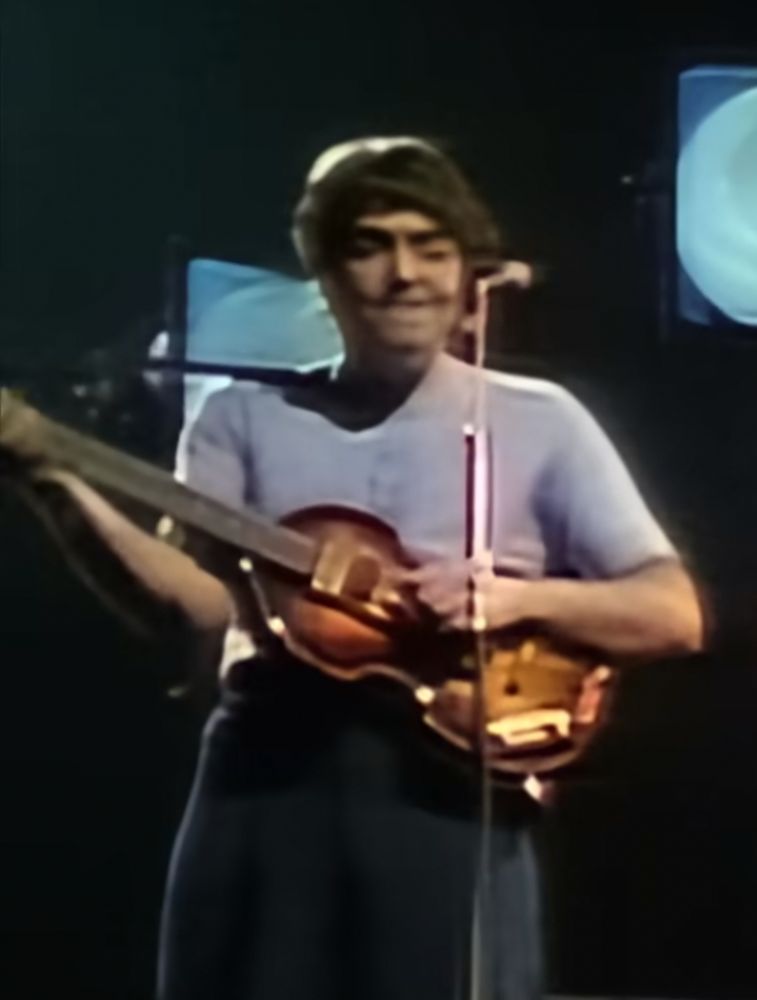 color screenshot from the "remastered" Beatles Anthology: AI upscaled version of Paul McCartney with blobby face, hair merging into something behind him, mic stand melding with hand. His face is distorted in an indescribable way.