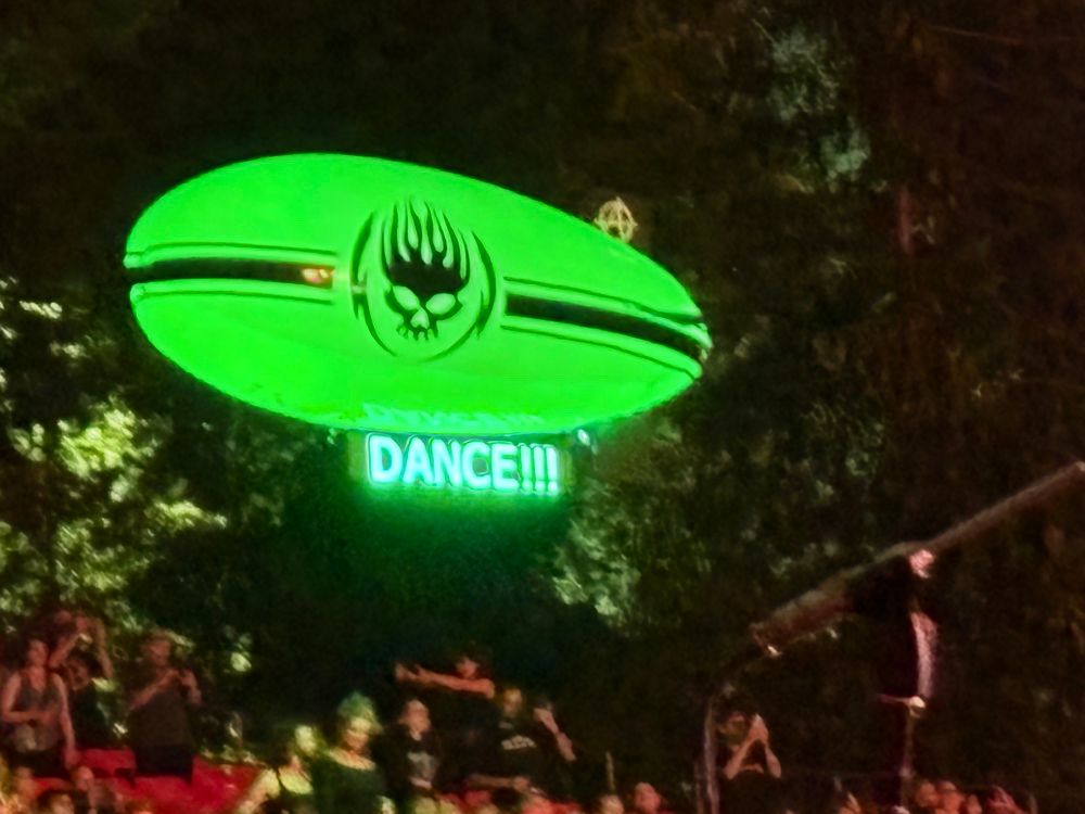 A neon green blimp with a black The Offspring logo in the middle floats above the crowd. Below, an LED signboard says dance ( if you’re a fan, you know the rest of the chorus) 