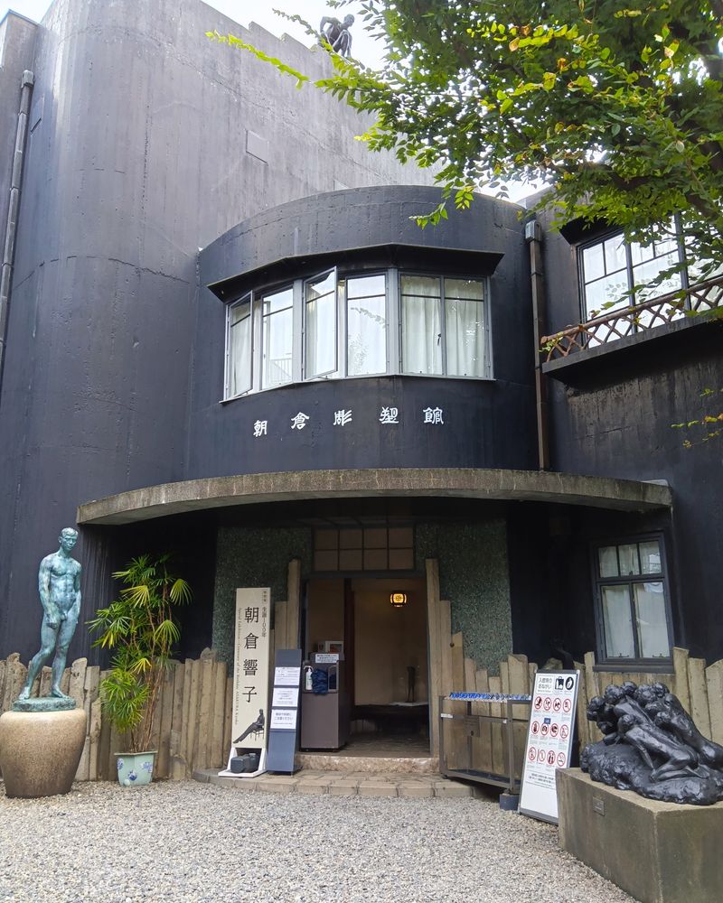 「朝倉彫塑館」入口外観

壁面が黒く塗られた立体的な構造の３階建てで、元は朝倉文夫のアトリエだった建物
入口の左右に、朝倉文夫の作品が１点ずつと、朝倉響子展の案内看板が置かれている
屋上にも彫塑作品があるのがちらっと見える