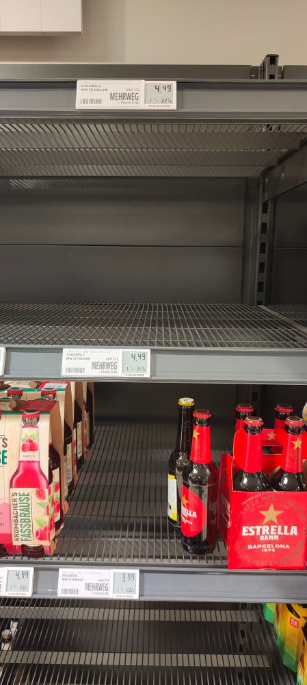 Regal-Stellplätze bei REWE. Es sind nur wenige alkoholfreie Getränke vorhanden. Man erkennt malzbier-bezogene Preisschilder. Die Fächer, in denen normalerweise Malzbier angeboten wird, sind komplett leer. Auch alkoholfreies Bier und Radler ist kaum zu finden. Bei alkoholhaltigem Bier (nicht abgebildet) ist die Auswahl größer.