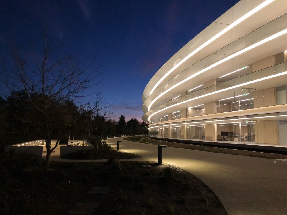 Apple Park in the early morning, the ring is lit against a dark blue sky
