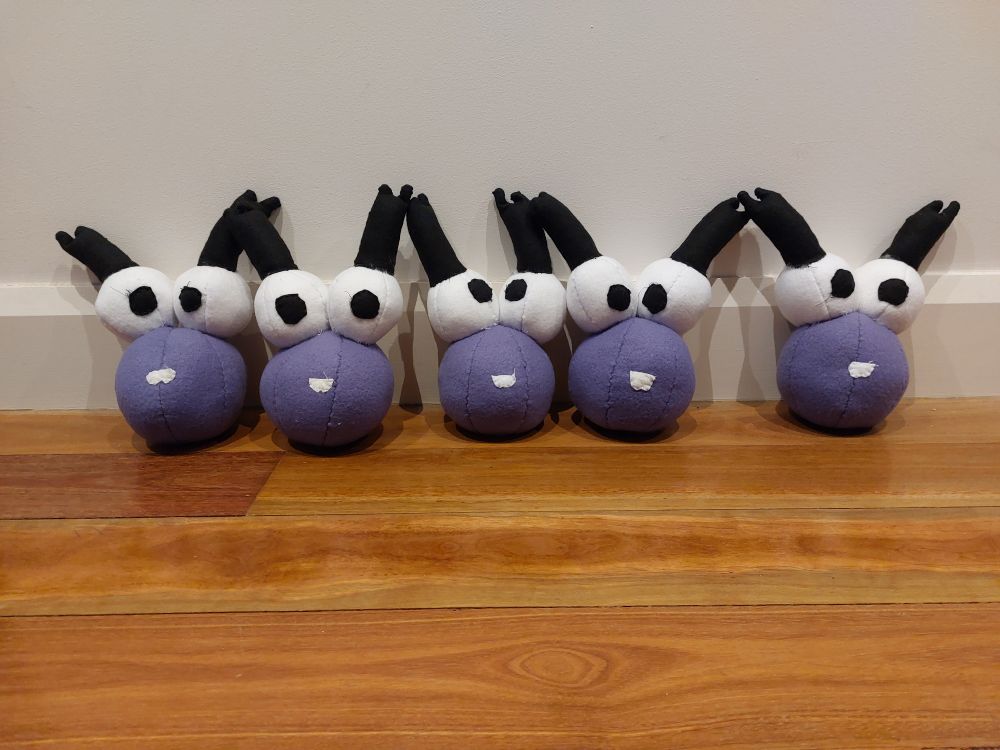 Five Koki (purple blob with big cartoon eyes and eye lashes) plushies lined up