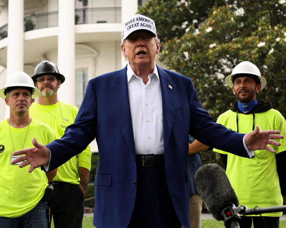 Yer man trump outside the White House with three blokes wearing hi-viz vests and workmen’s helmets around him.