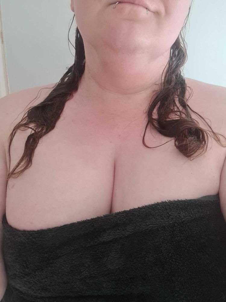 Woman with lip piercings, fresh out of the shower, wrapped in a black towel. 

