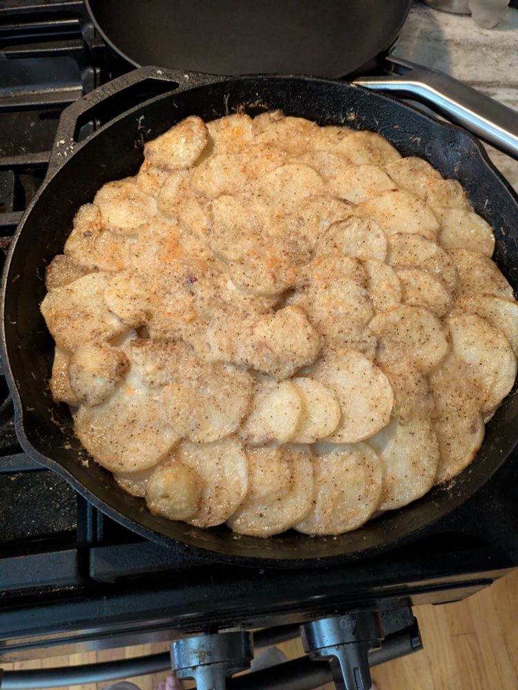A giant cacio e pepe potato cake I'm a cast iron pan on a stove 
