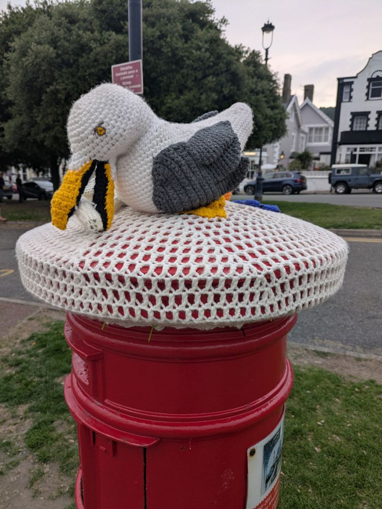 A crocheted seagull eating a crocheted fry atop a metal canister 