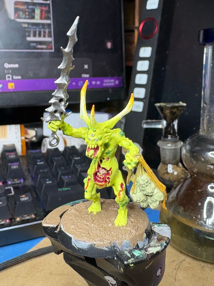 A bright green miniature with horns and a ripped open gut brandishing a thorny sword and carrying heads