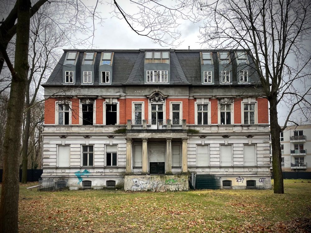 A stately looking home nine windows wide with big tall ceilings and a red-brick middle. Two of the windows are burned out after an apparent fire. 
