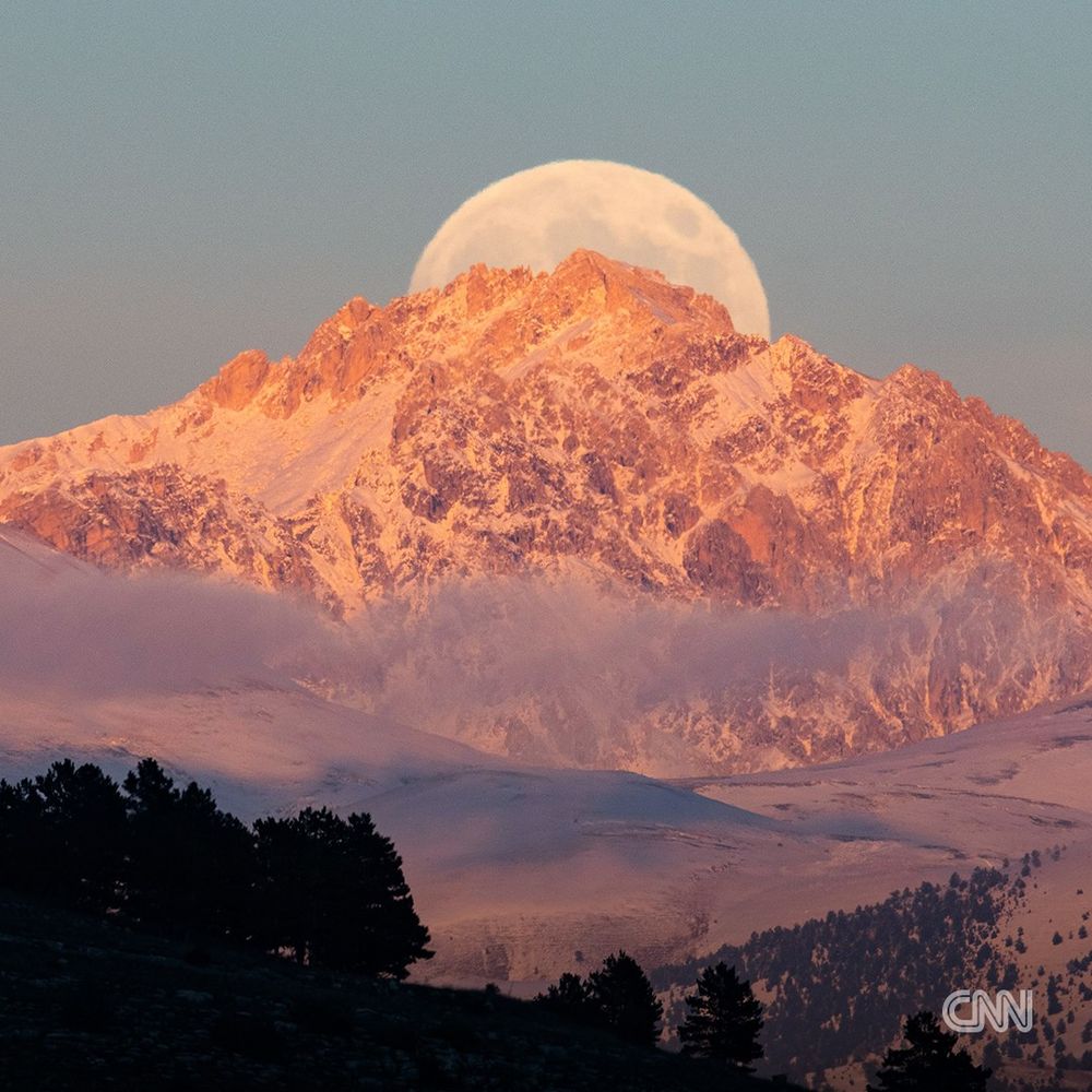 A full moon rising behind the rugged peaks of Monte Prena, seen from L'Aquila, Italy